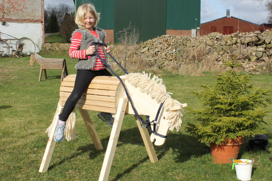 Kind reitet auf Holzpferd im Garten