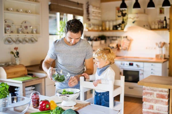 Vater und Kind kochen gemeinsam. Das Kind nutzt einen Lernturm