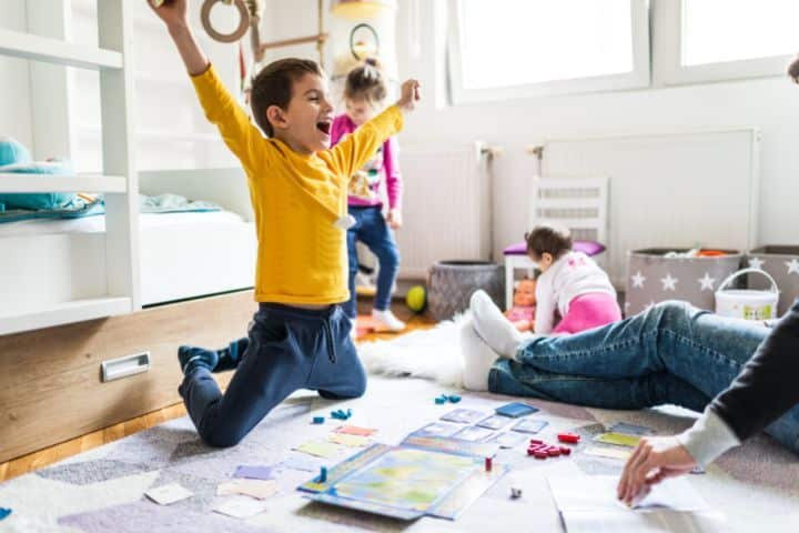 7-jähriger Junge jubelt über seinen Sieg bei einem Gesellschaftsspiel im Kinderzimmer